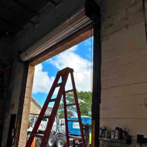 View through open warehouse door past a red ladder.